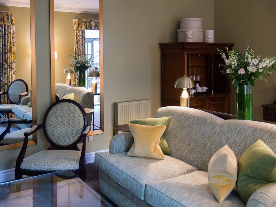 A living room with a sofa, armchairs, a glass coffee table, and a mirror.