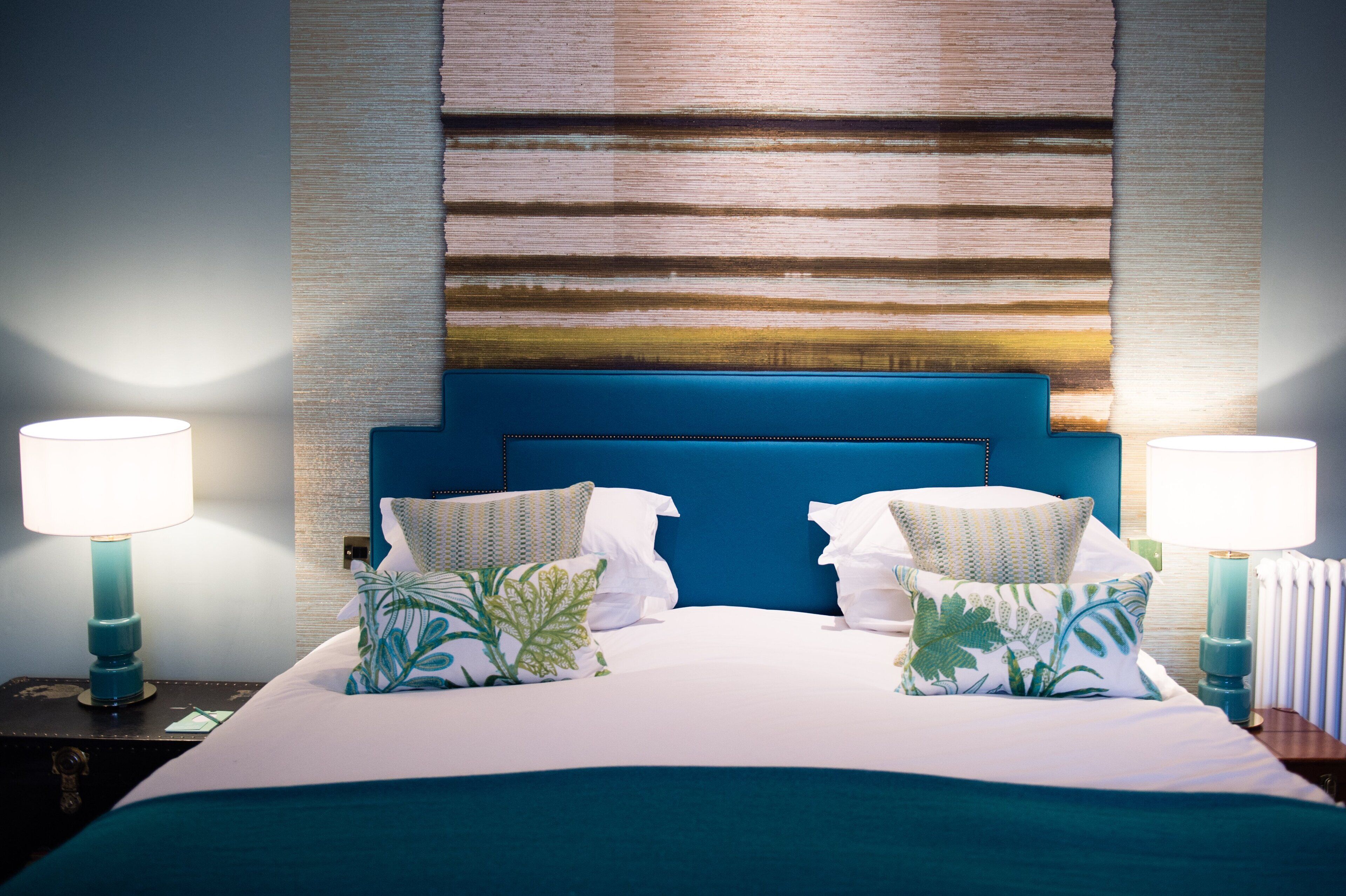 Quarto de hotel com uma cama grande, cabeceira azul e duas luminárias laterais.
