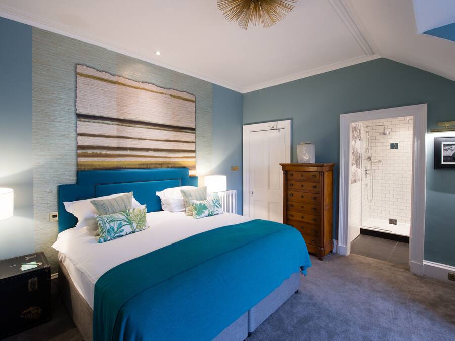 A bedroom with a large bed, a dresser, a nightstand, and a bathroom with a shower and toilet visible.