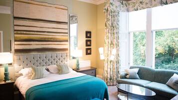 A hotel room with a large bed, a sofa, a coffee table, and a view of greenery outside.