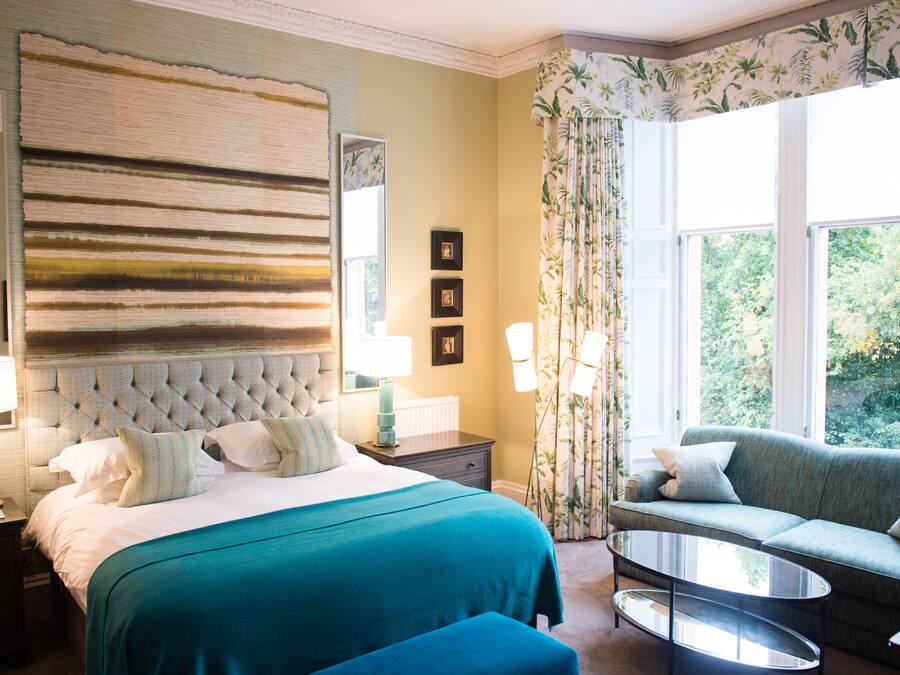 A hotel room with a large bed, a sofa, a coffee table, and a view of greenery outside.