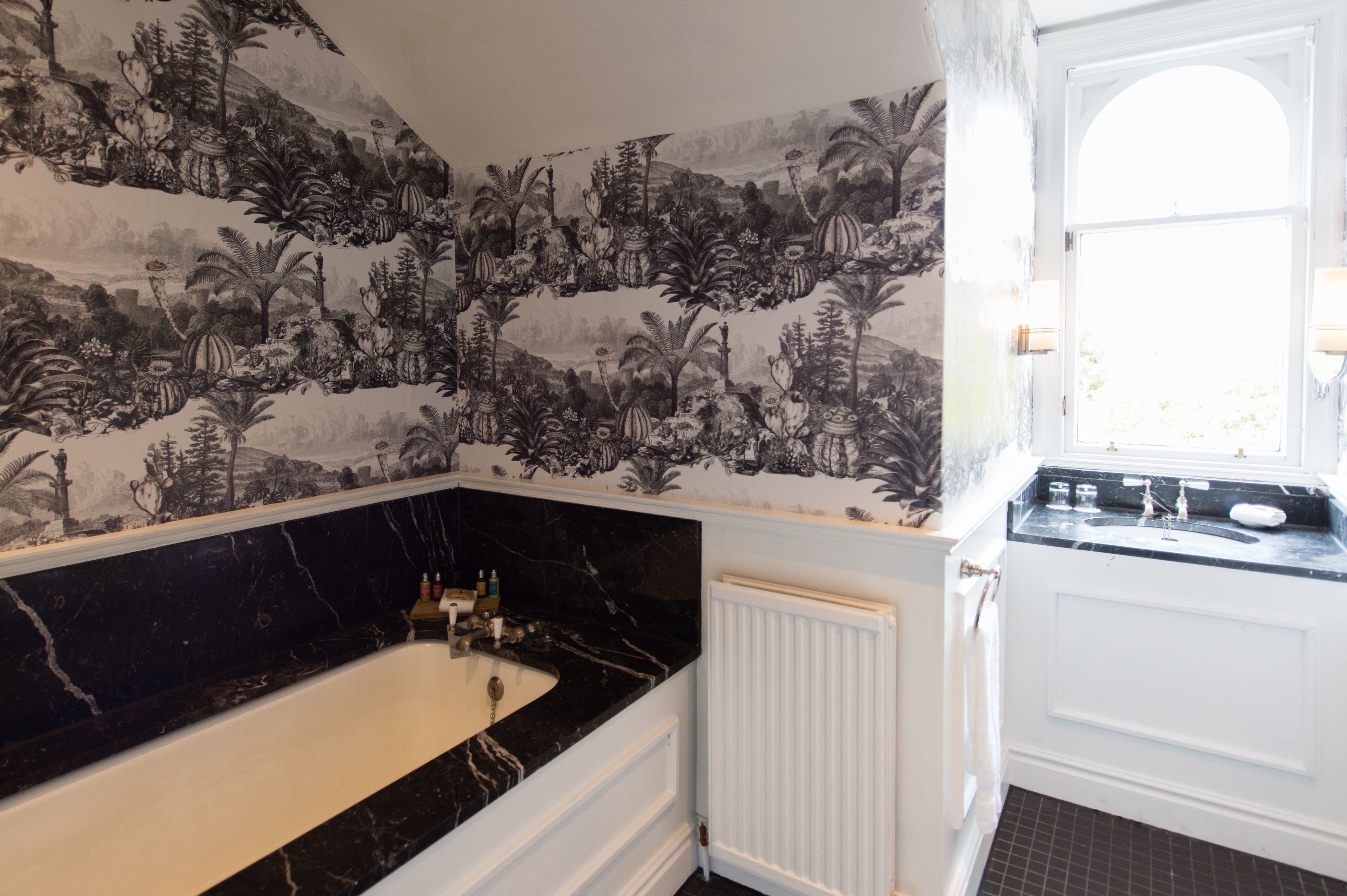 Une salle de bain avec un papier peint à motifs noir et blanc, une baignoire en marbre et un radiateur blanc.