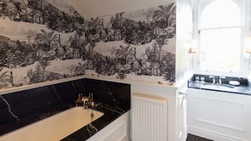 Une salle de bain avec un papier peint à motifs noir et blanc, une baignoire en marbre et un radiateur blanc.