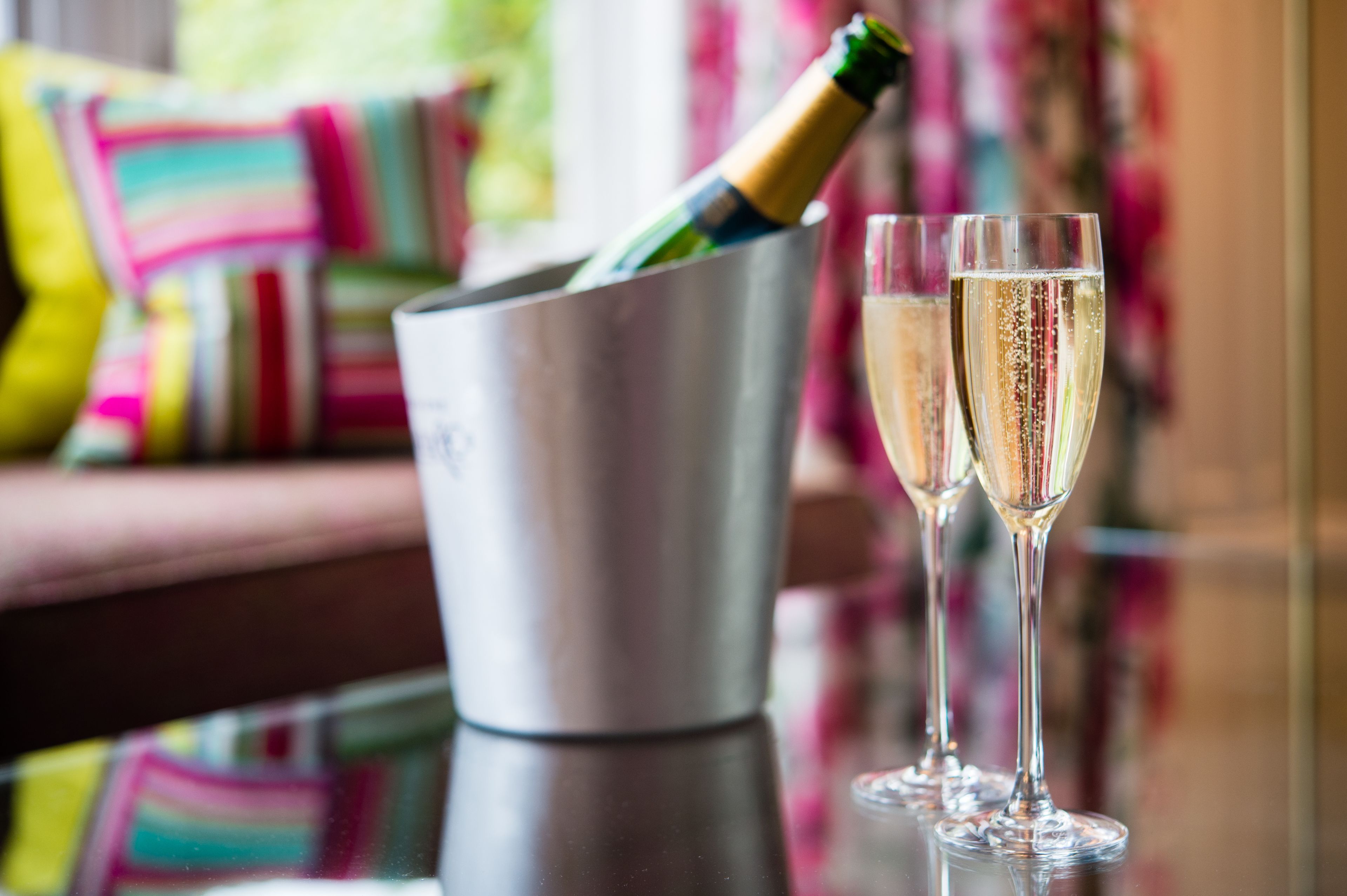 A champagne bottle in a metal bucket with two glasses of champagne on a reflective surface.