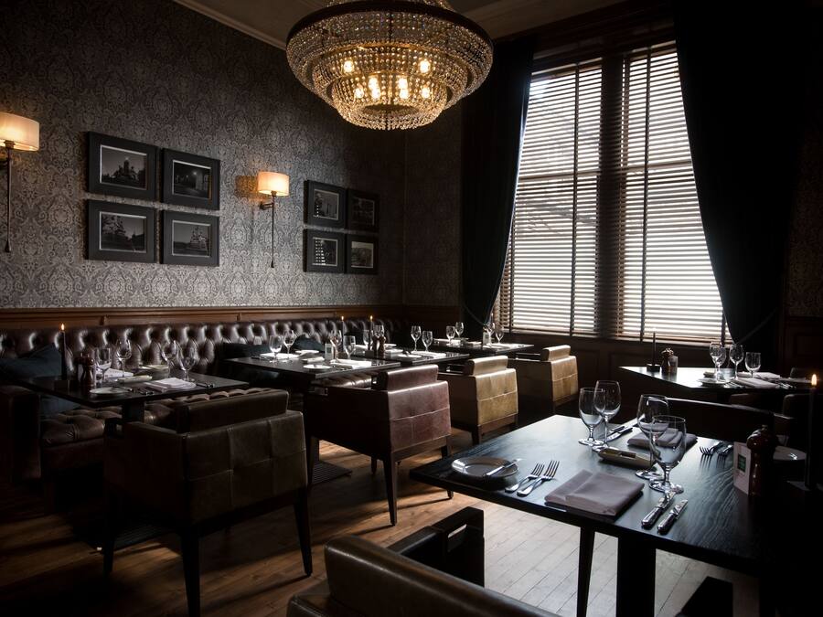 A dimly lit restaurant with a classic chandelier, leather booths, and framed pictures on the wall.