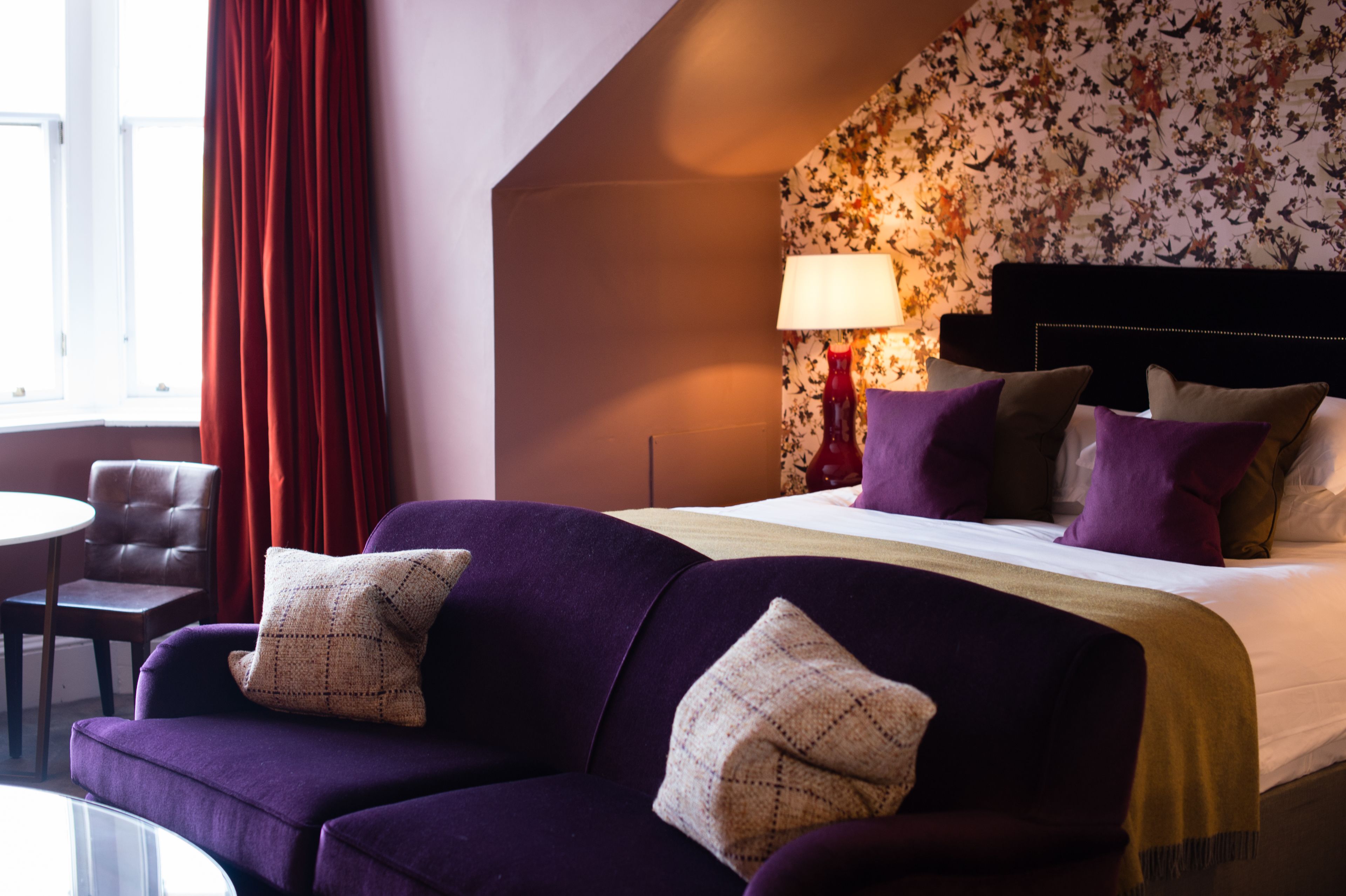Una habitación de hotel con una cama, sofá púrpura y cortina roja.
