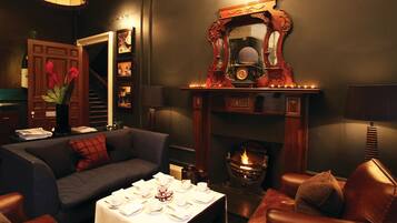 A cozy living room with a fireplace, a sofa, a table set for dining, and a decorative mirror.