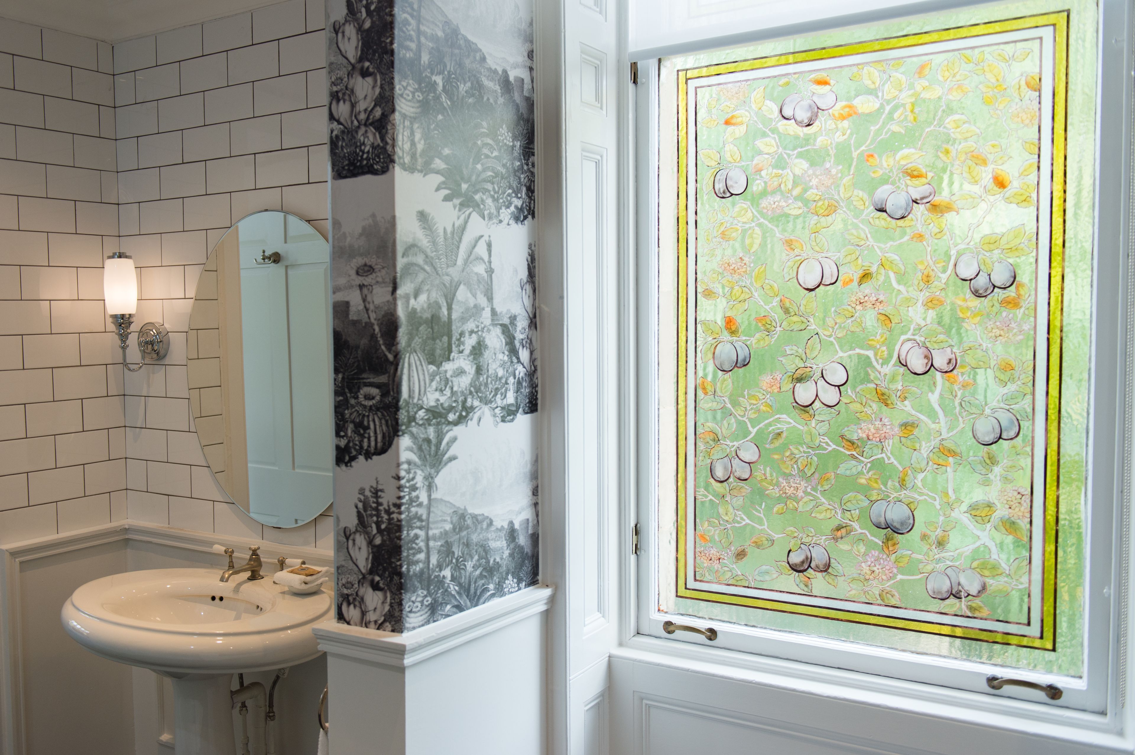 A bathroom with a white sink, a wall-mounted mirror, and a decorative panel with a fruit pattern.