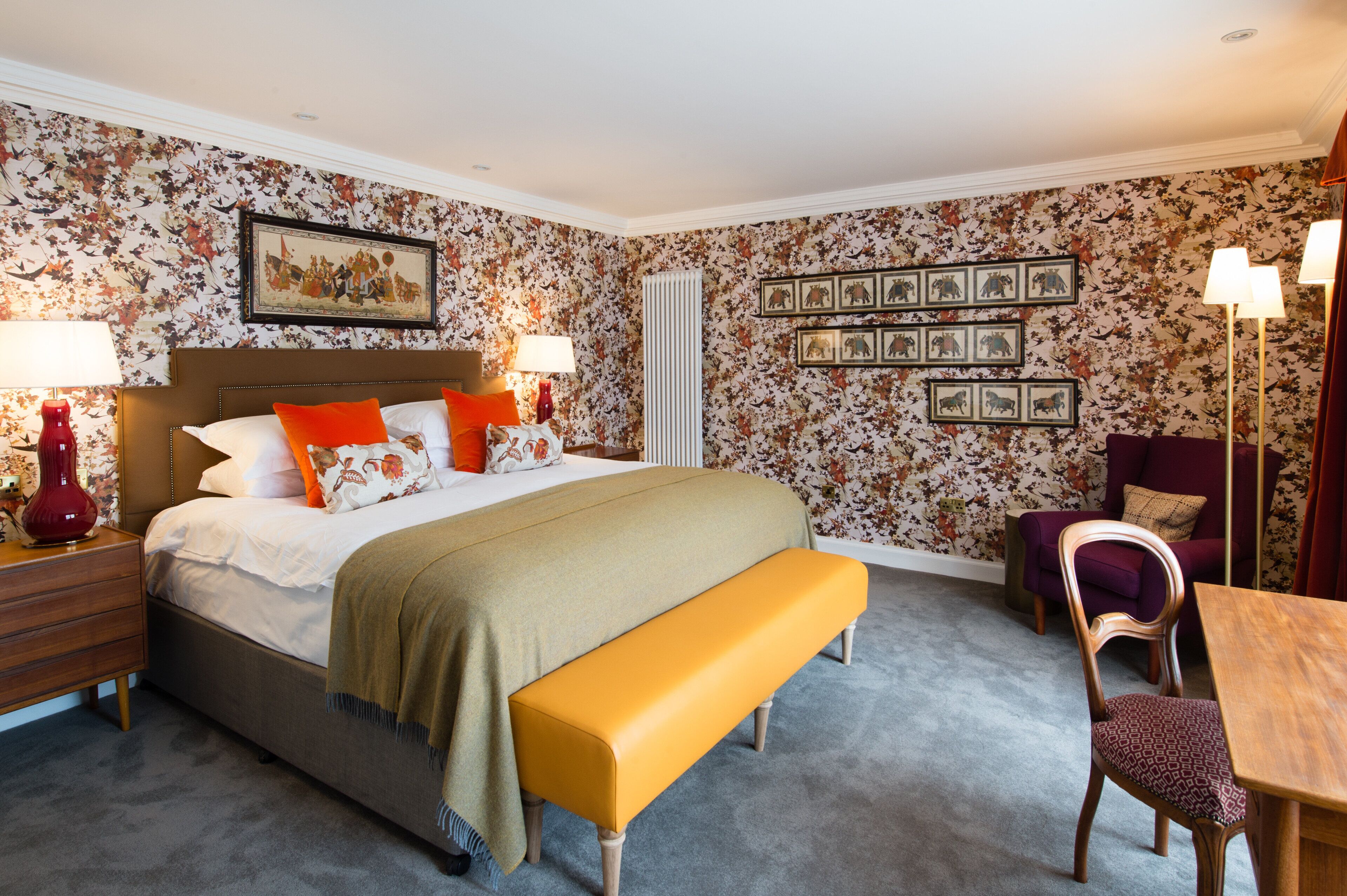 A bedroom with a bed, bedside tables, a bench, a chair, a table, and wall-mounted picture frames.