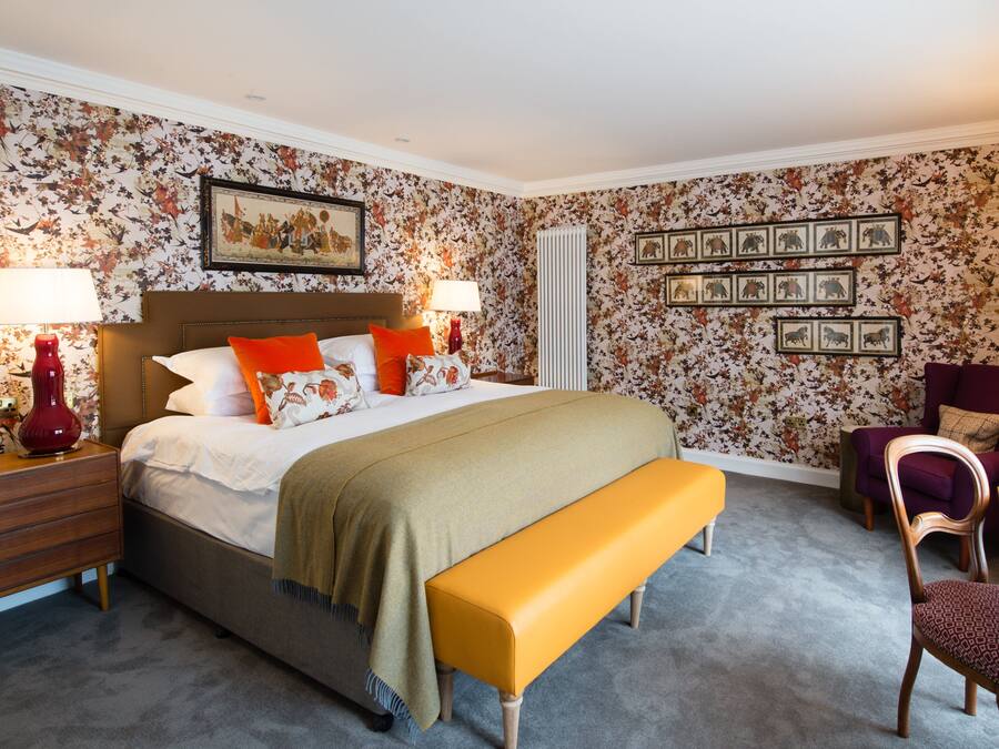 Een slaapkamer met een bed, nachtkastjes, een bankje, een stoel, een tafel en wanddecoratie.