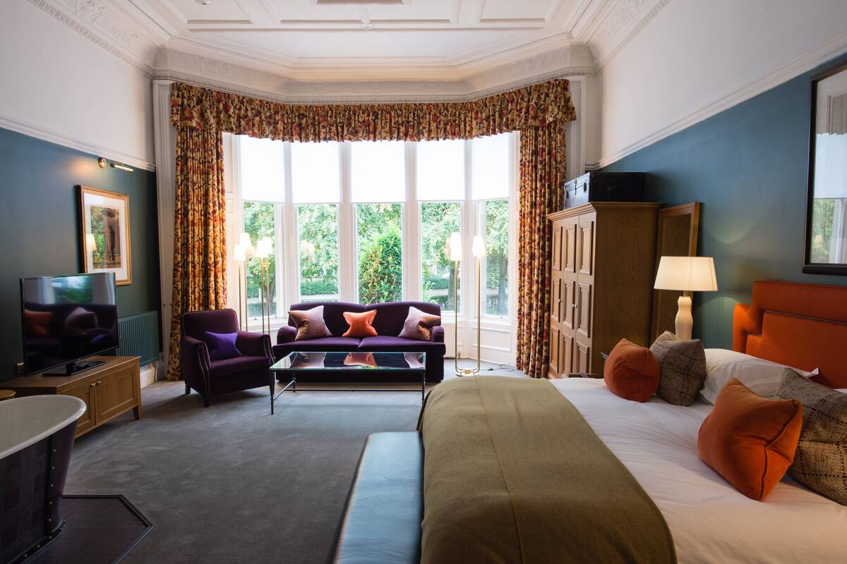 A hotel room with a bed, a sofa, a television, and a desk.