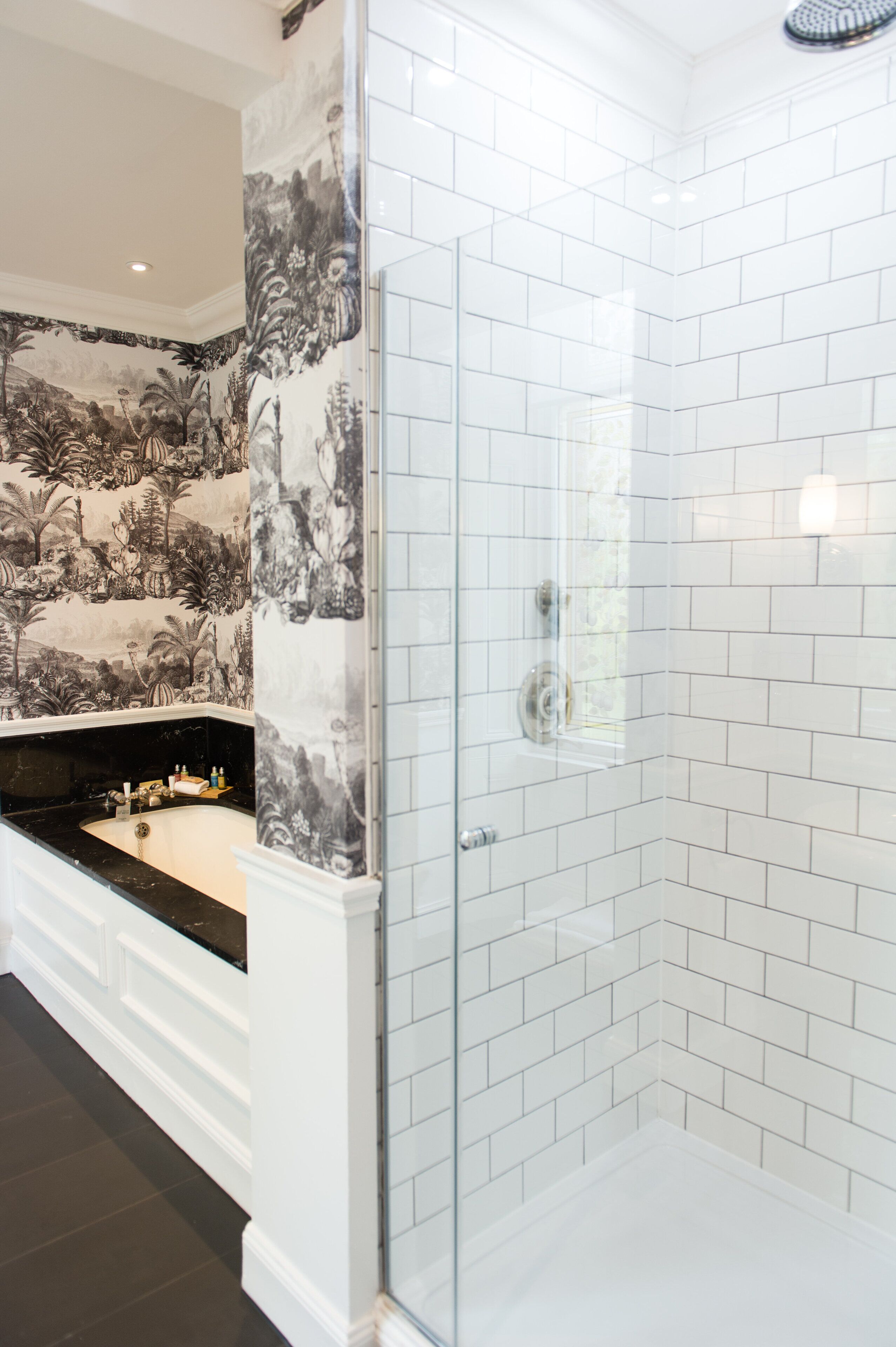 A bathroom with a glass shower enclosure, white subway tiles, and a black bathtub with a white vanity.