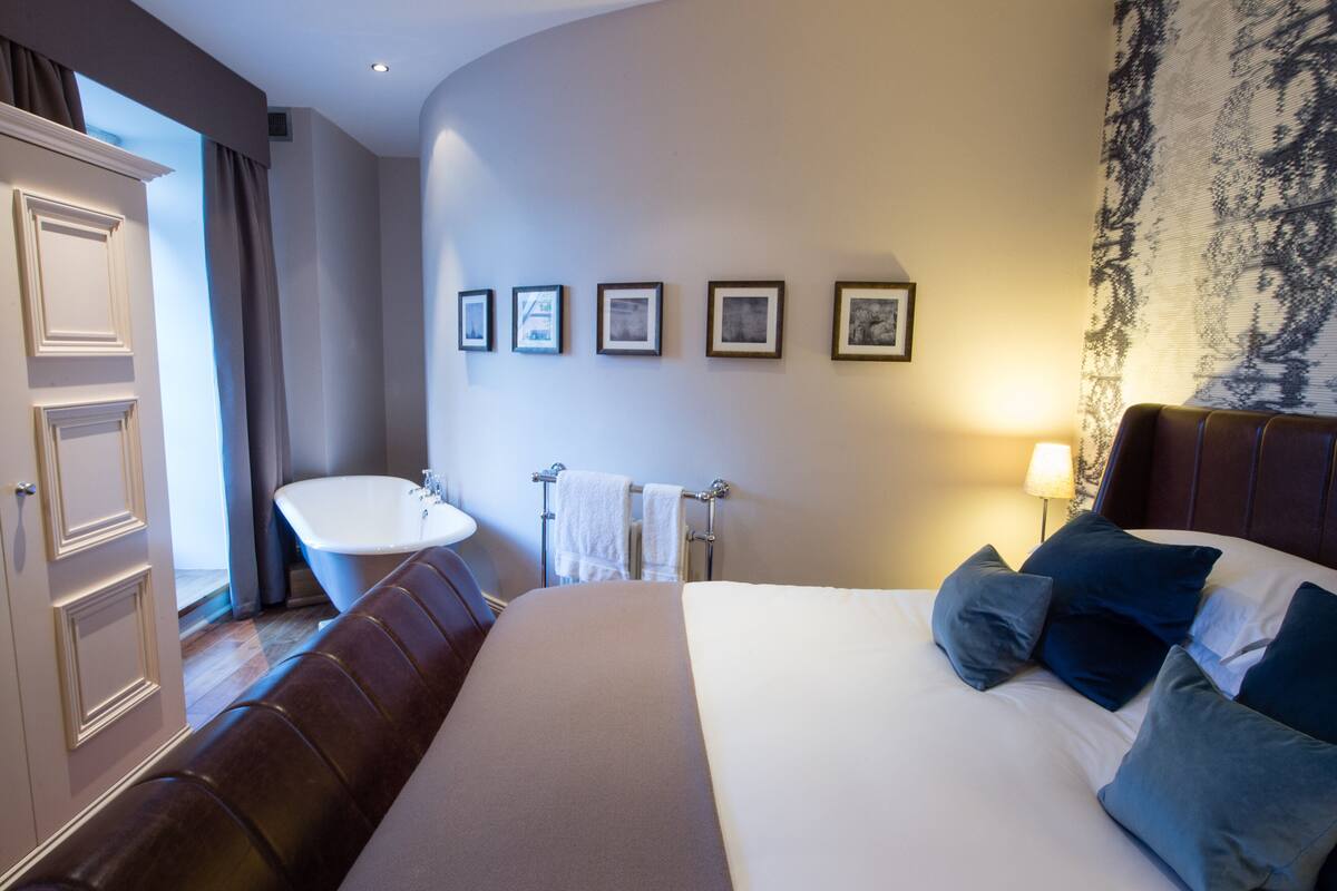 A hotel room with a large bed, a sitting area, a bathroom with a bathtub, and framed pictures on the wall.