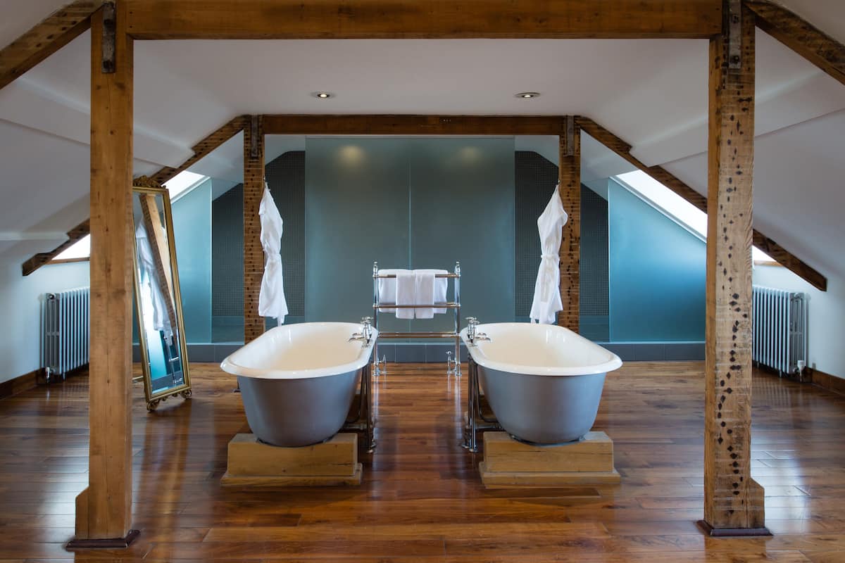 A room with two large tubs under a sloped ceiling, wooden beams, and a mirrored wall.