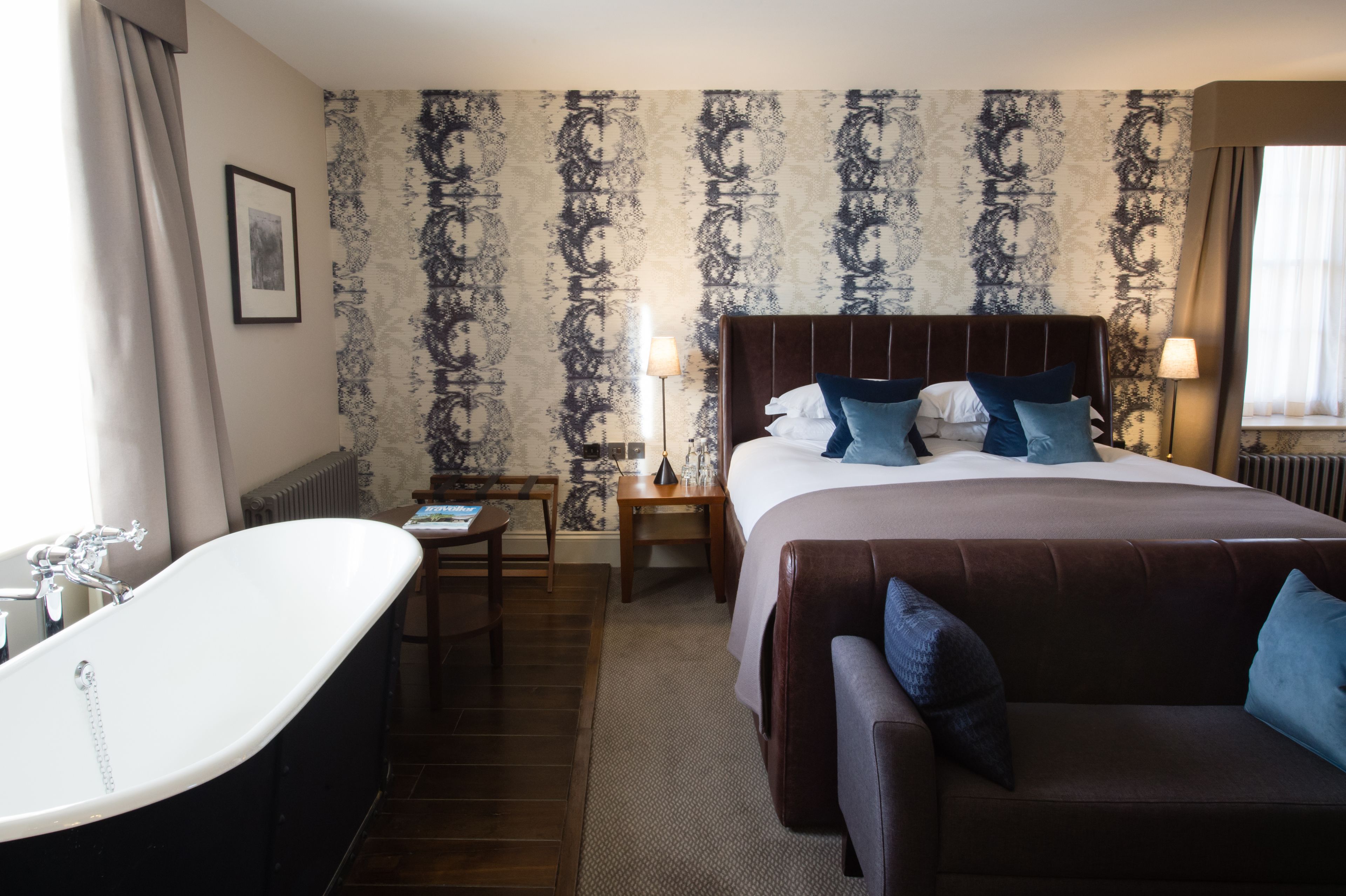 A hotel room with a large bed, a sitting area with a sofa, a bathtub, and a patterned wallpaper.
