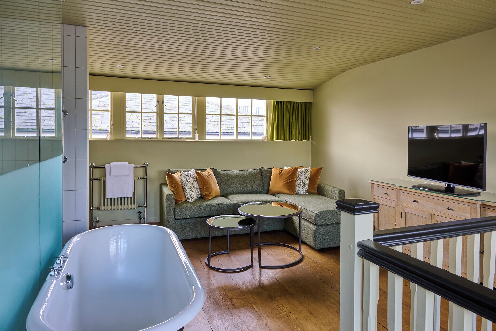 Een moderne woonkamer met een groot bad, een hoekbank, een glazen salontafel en een televisie op een houten dressoir.