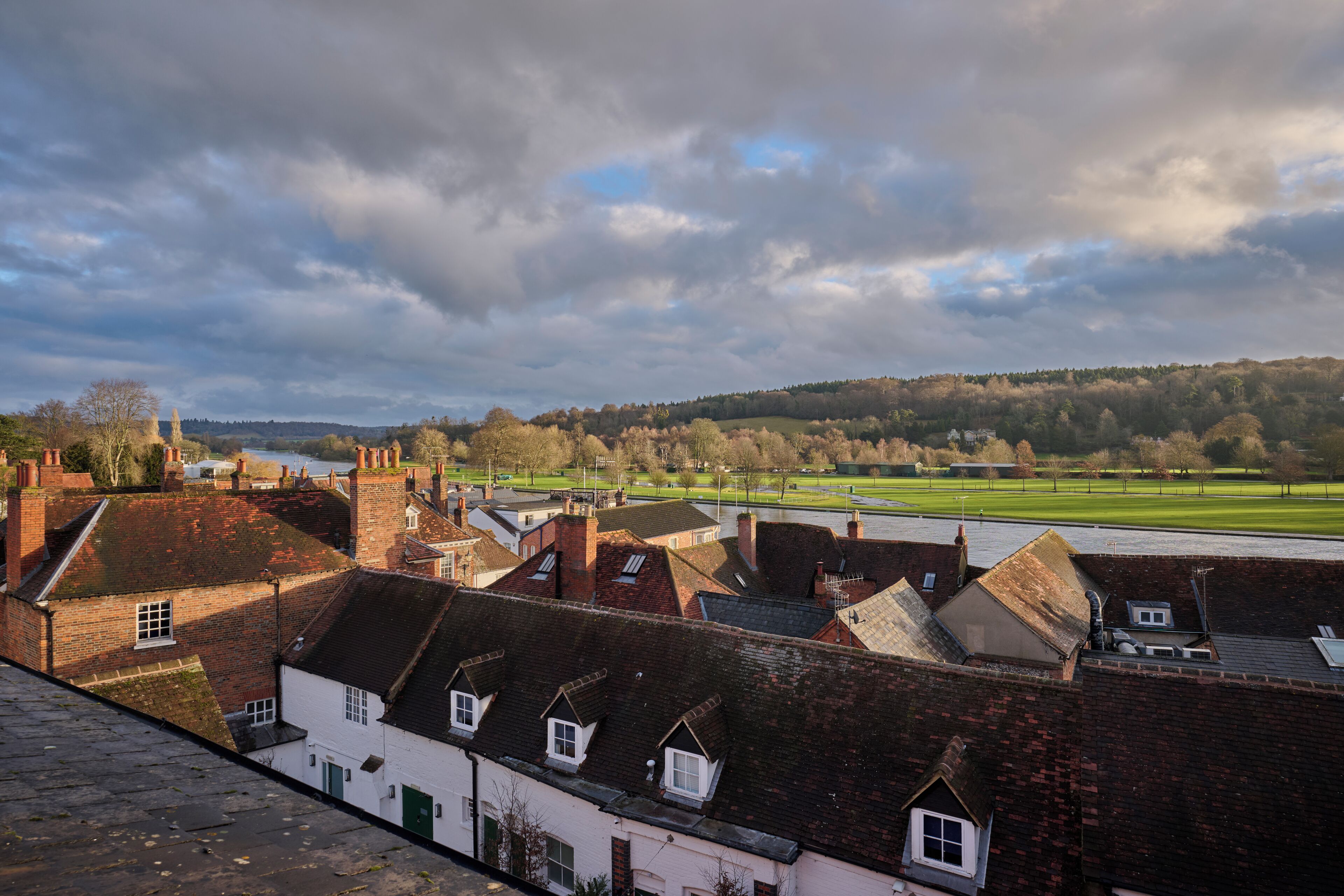 A view of a town with traditional brick buildings, a river, and a green field in the distance.