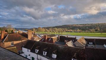 A view of a town with traditional brick buildings, a river, and a green field in the distance.