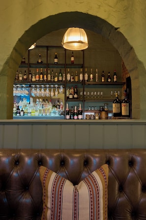 A bar area with shelves of bottles and glasses, a cushioned seating area, and a hanging light fixture.