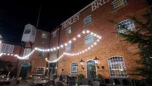 A brick building with the name "HENLEY BREWER" on the side, outdoor seating with tables and chairs, and string lights.