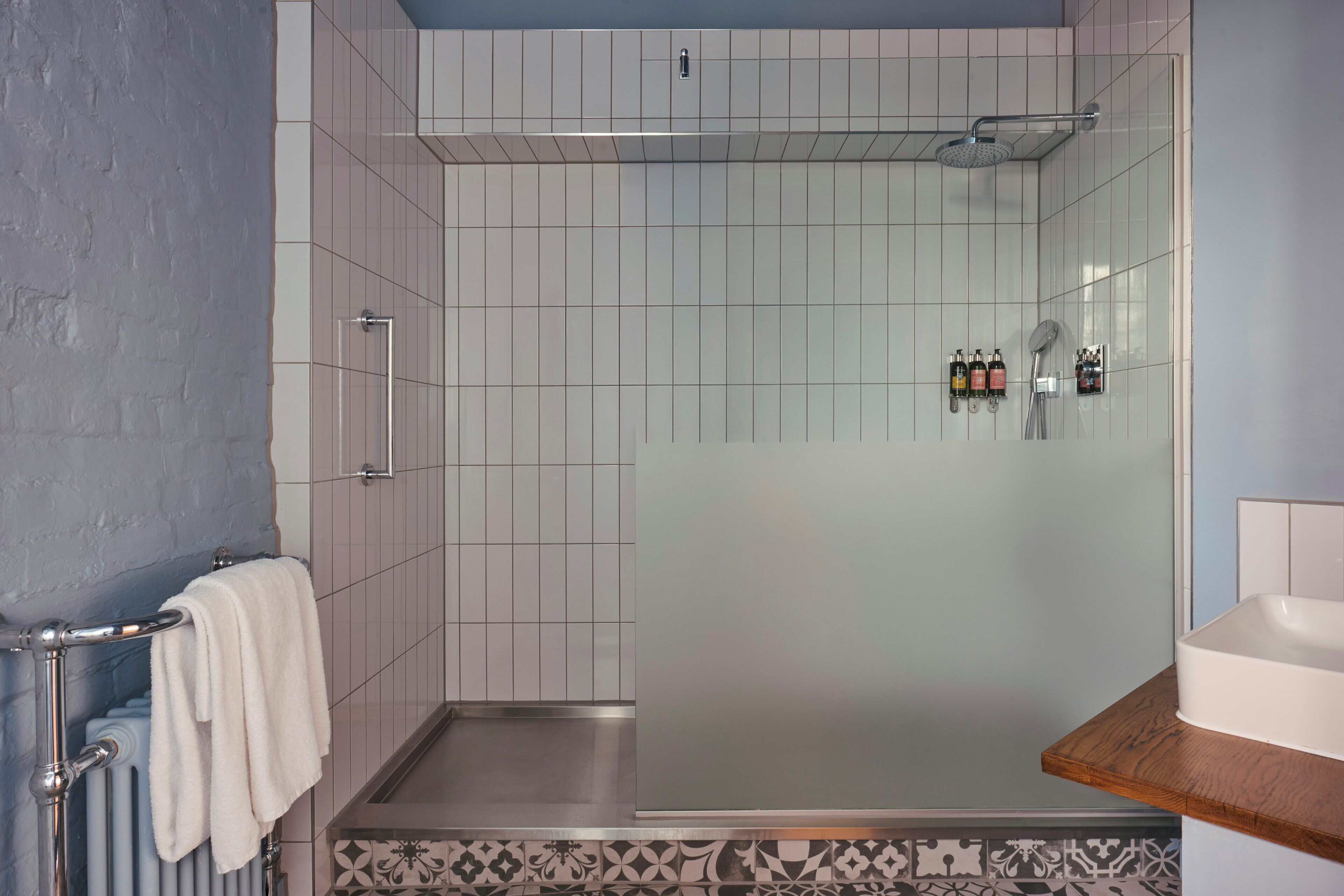 Un baño moderno con ducha de vidrio, un lavabo blanco y un perchero para toallas.