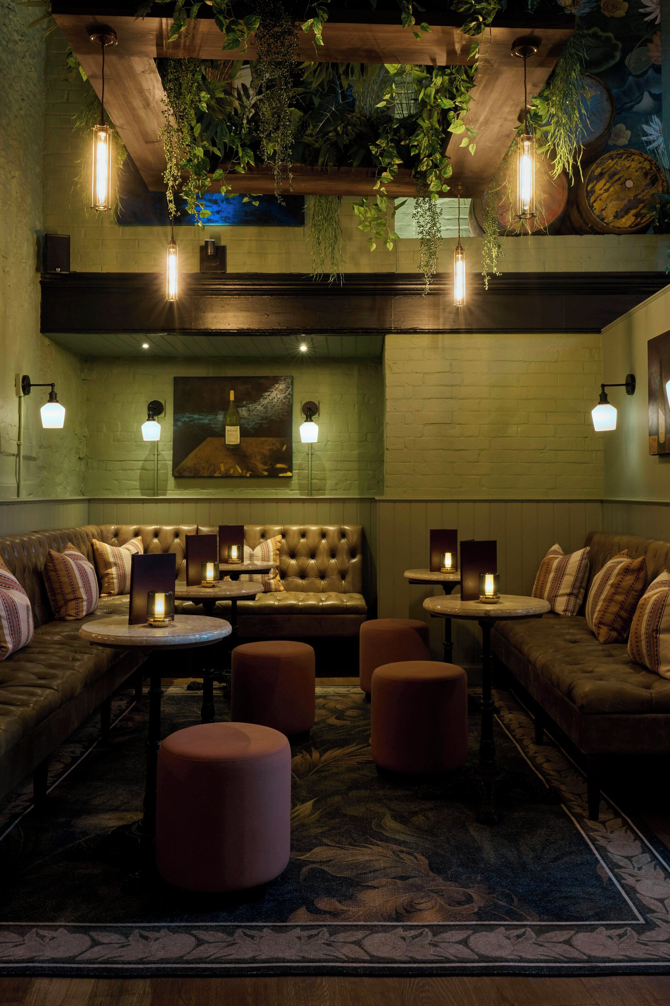 Un rincón lounge acogedor con sofás de cuero, mesas redondas y plantas colgantes.