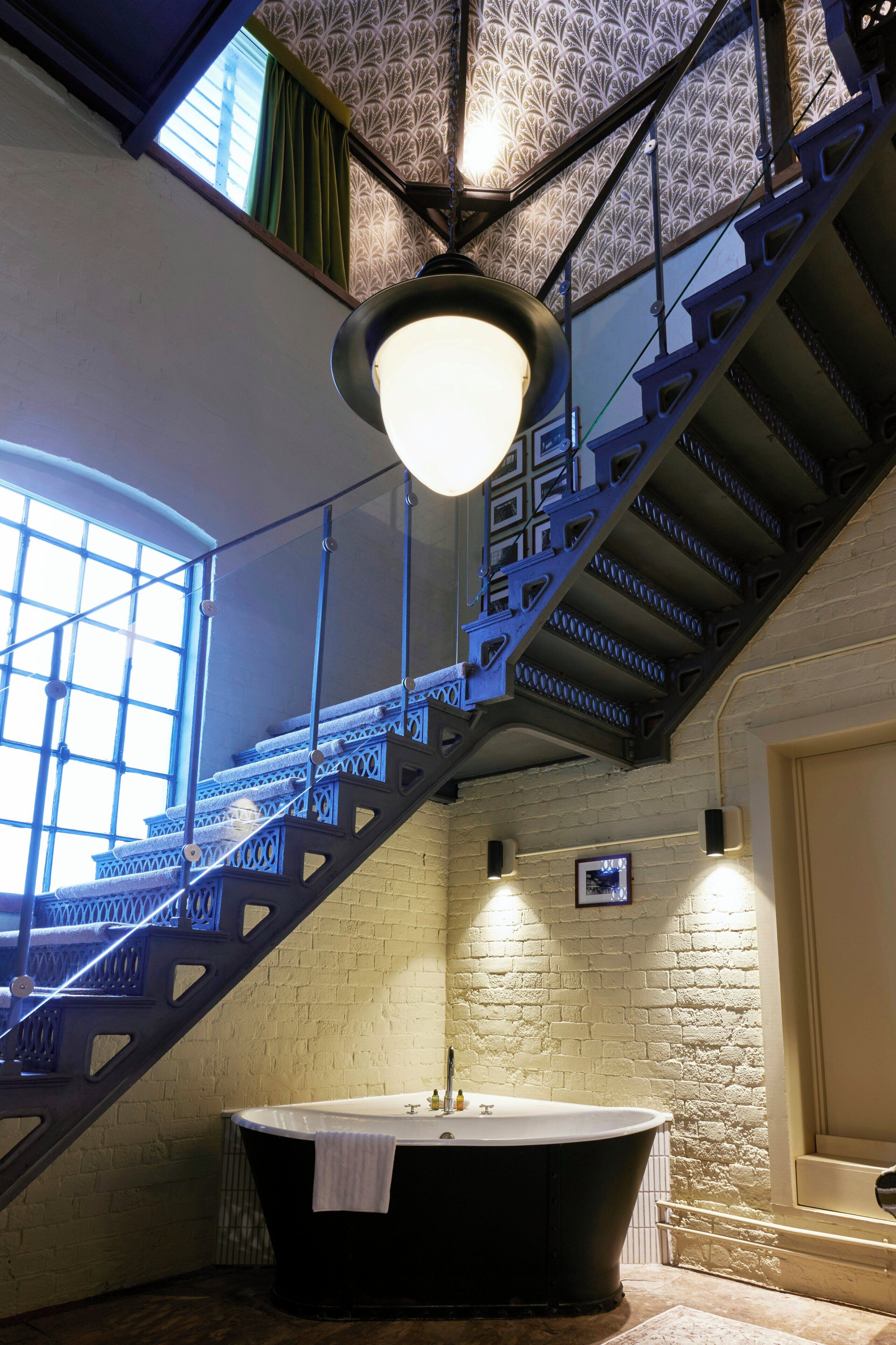 A bathroom with a freestanding bathtub, a staircase with decorative metal railings, and a patterned ceiling.