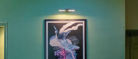 A framed poster of a woman with grapes on a teal wall, a skylight, and a staircase with wooden railings.