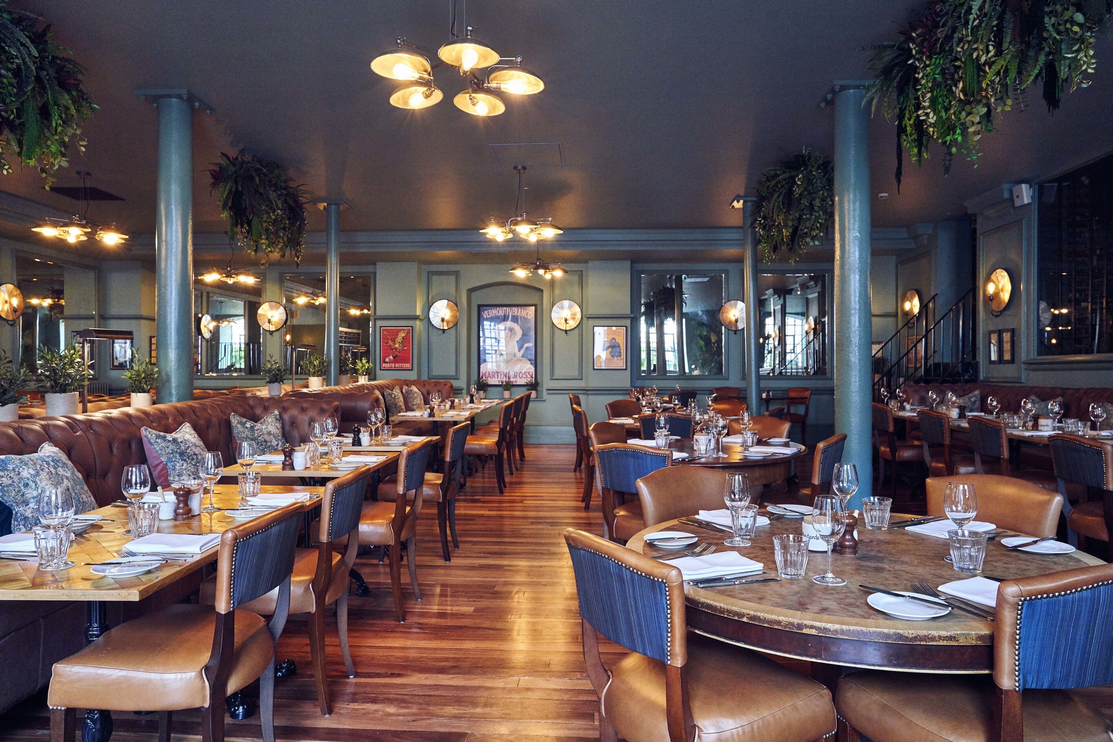 A spacious restaurant with high ceilings, hanging plants, and multiple dining areas.
