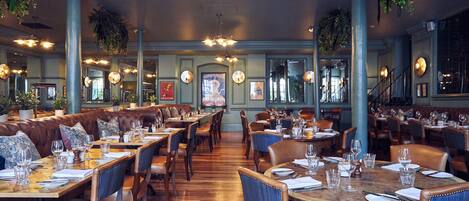 A spacious restaurant with high ceilings, hanging plants, and multiple dining areas.
