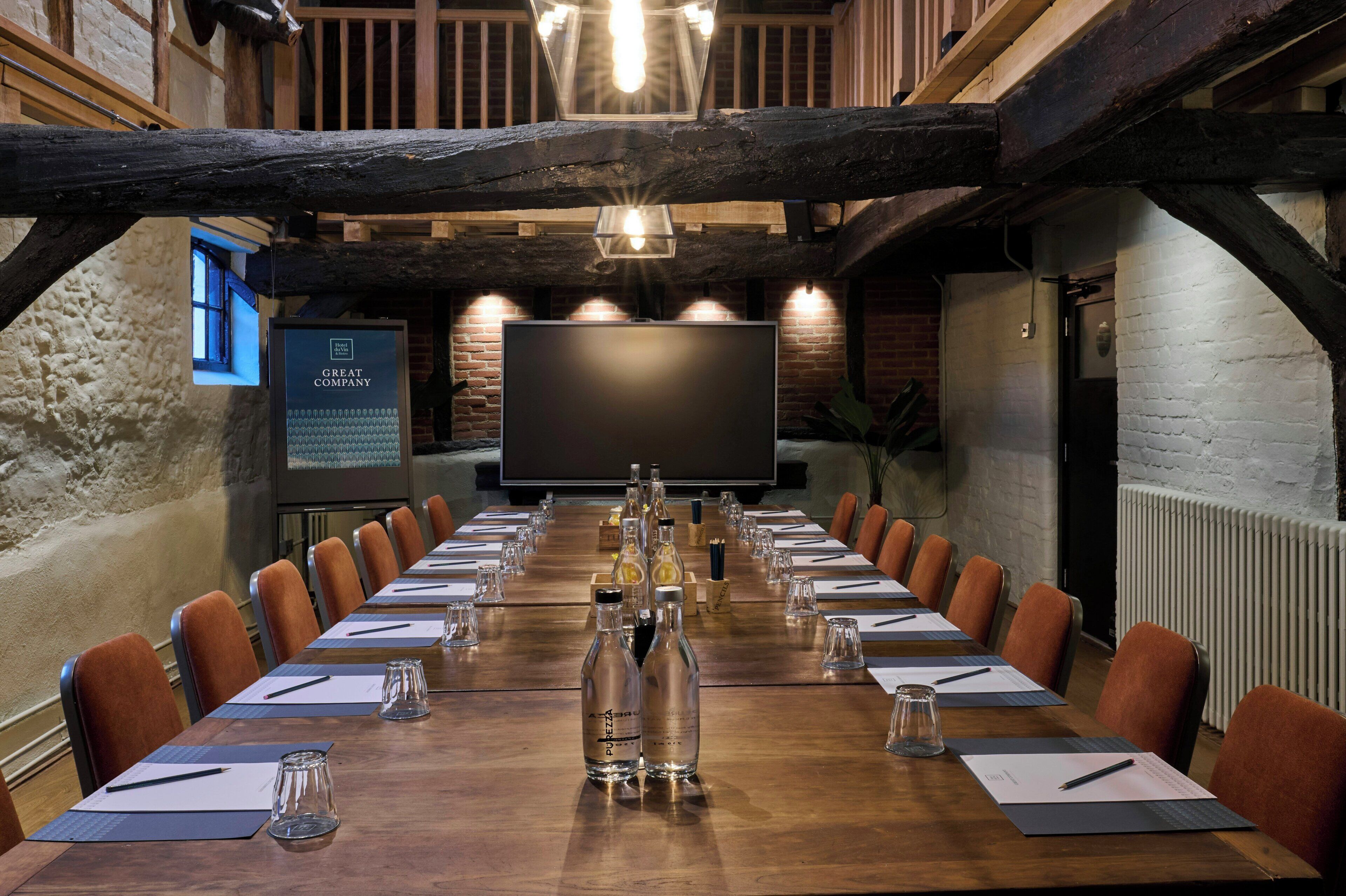 A conference room with a long table, brown chairs, and a large screen at the front.