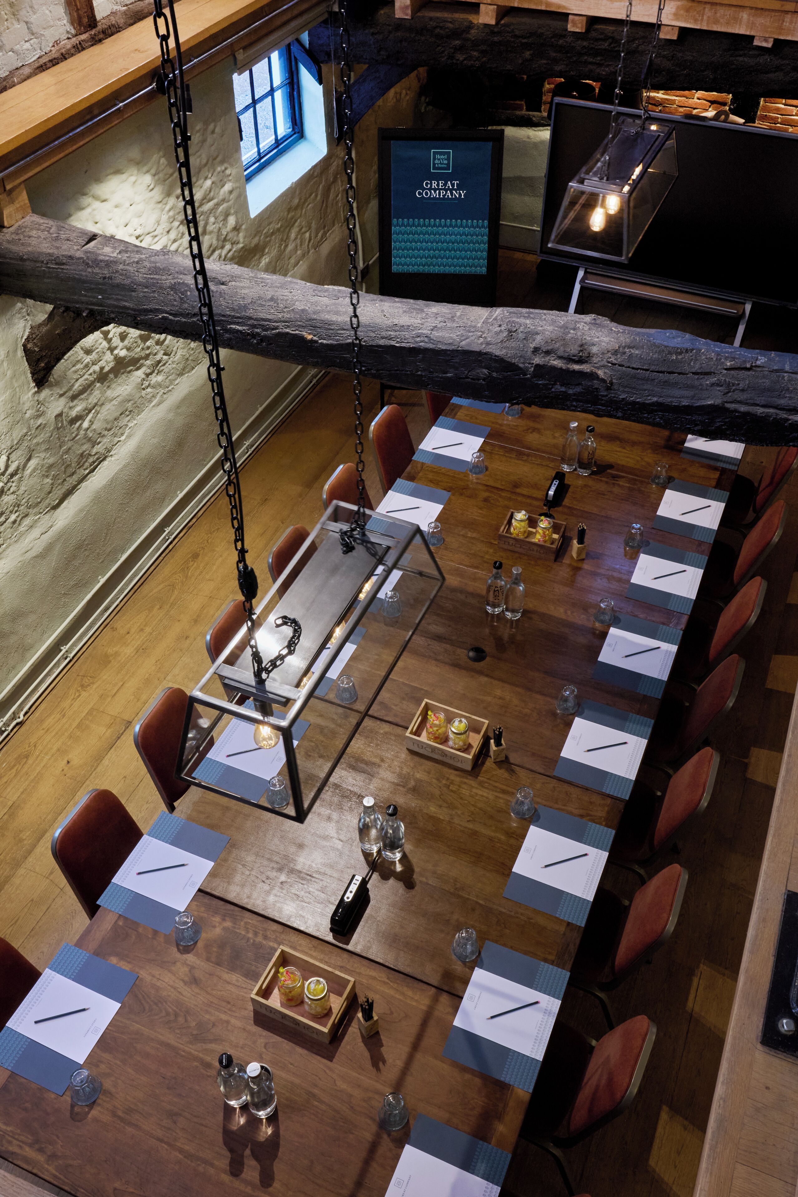 A long dining table with chairs, a hanging light fixture, and a wooden beam overhead.