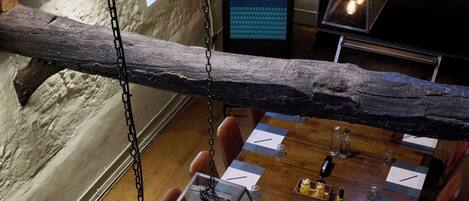 A long dining table with chairs, a hanging light fixture, and a wooden beam overhead.