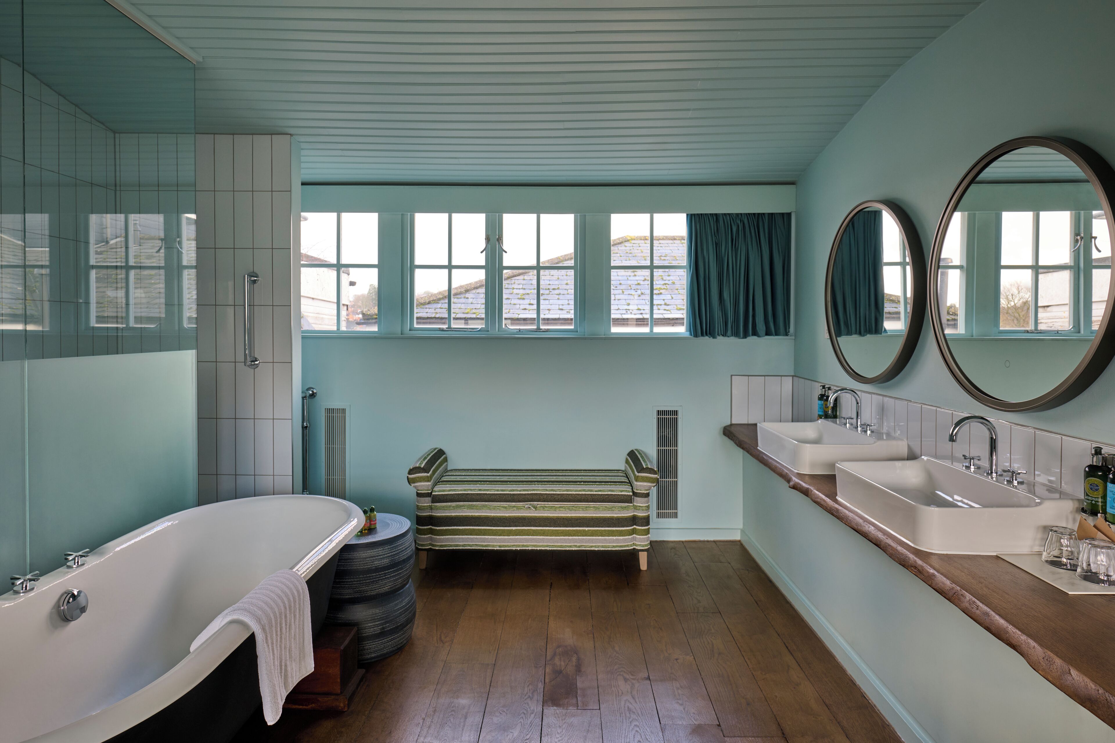 Ein Badezimmer mit einer Badewanne, einer Sitzbank, zwei Waschbecken und einem großen Spiegel.