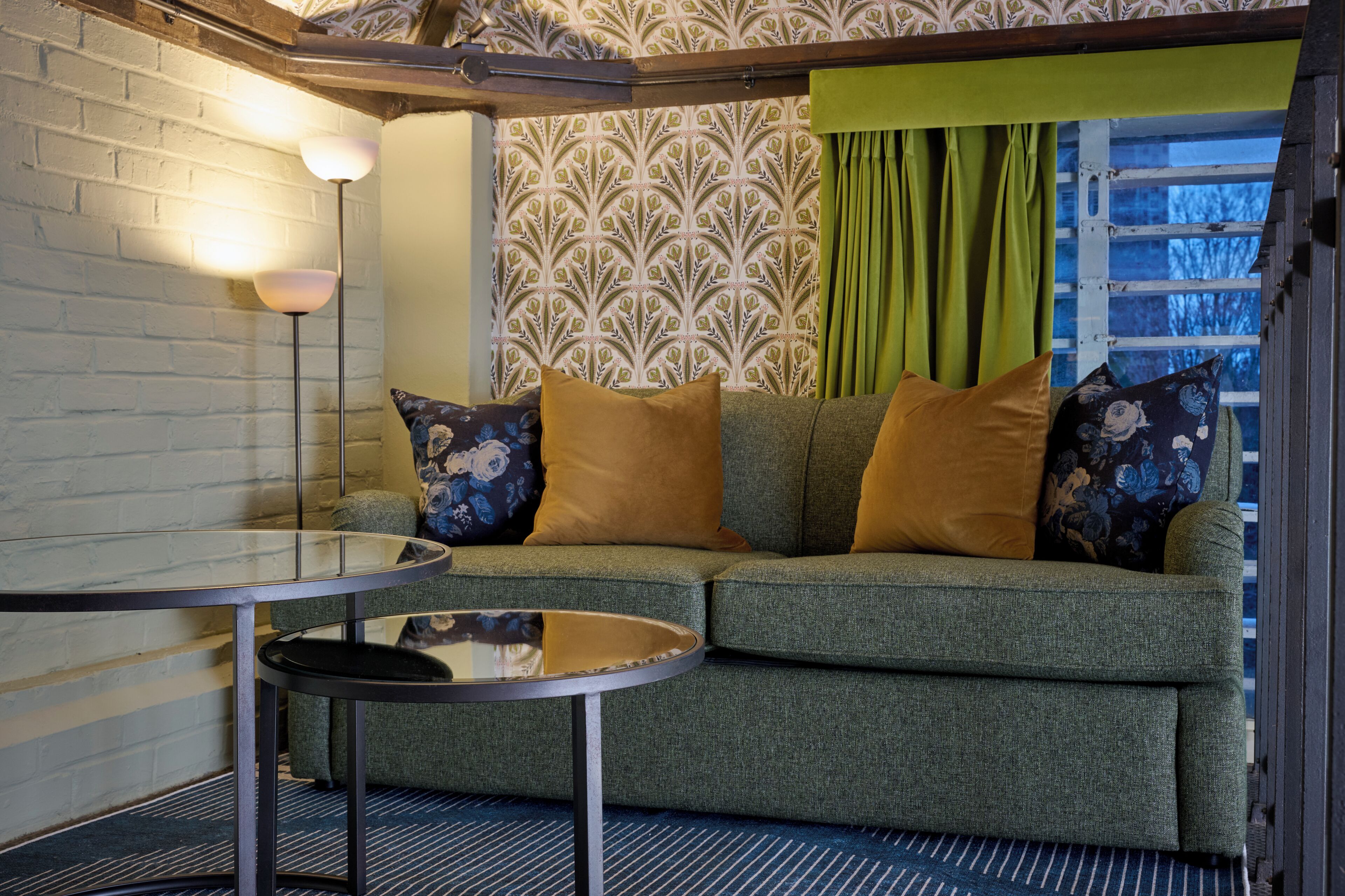 A cozy room with a green sofa, a round glass table, and patterned wallpaper.