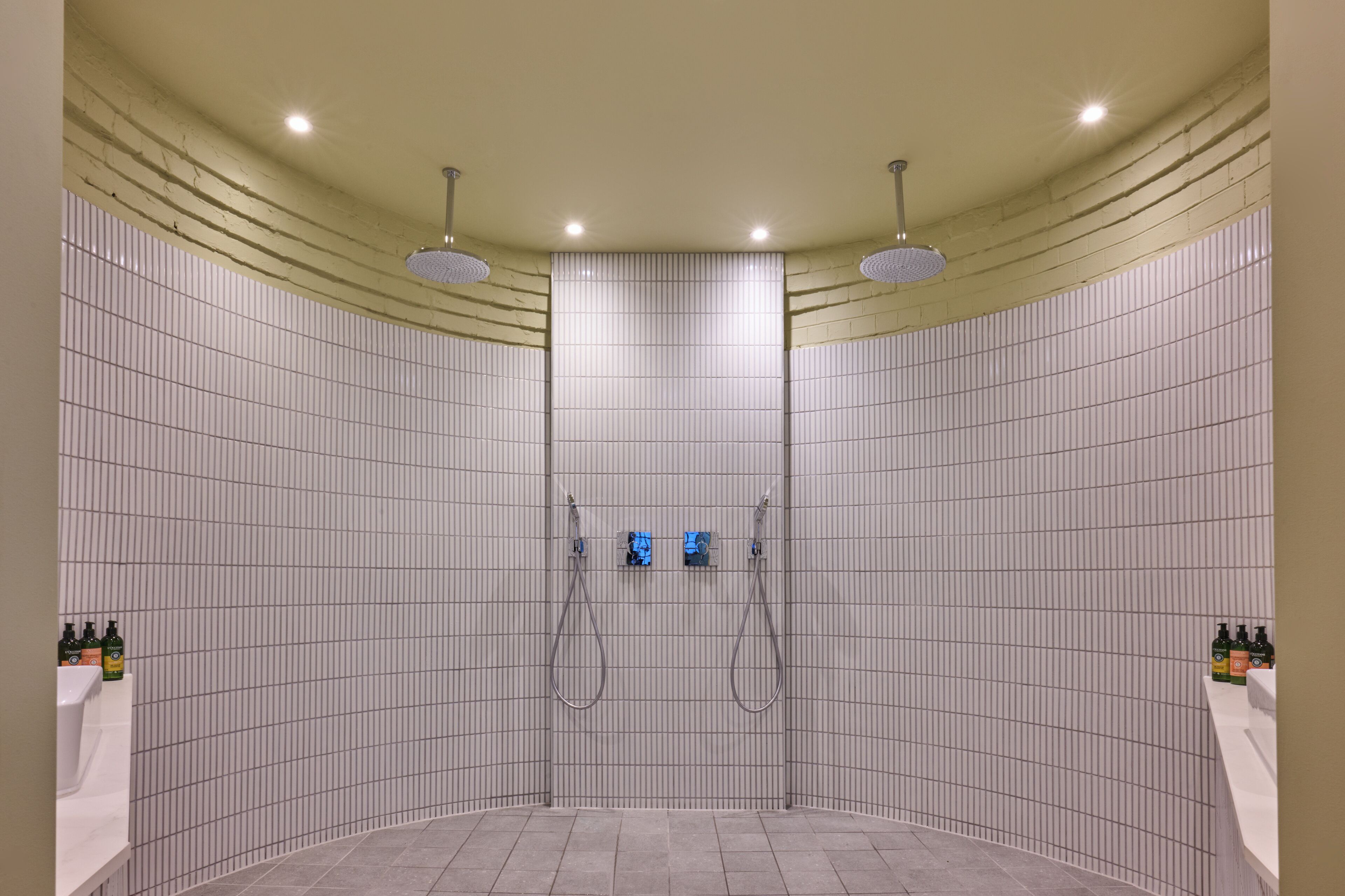 A modern shower area with a curved ceiling, recessed lighting, and a tiled wall.