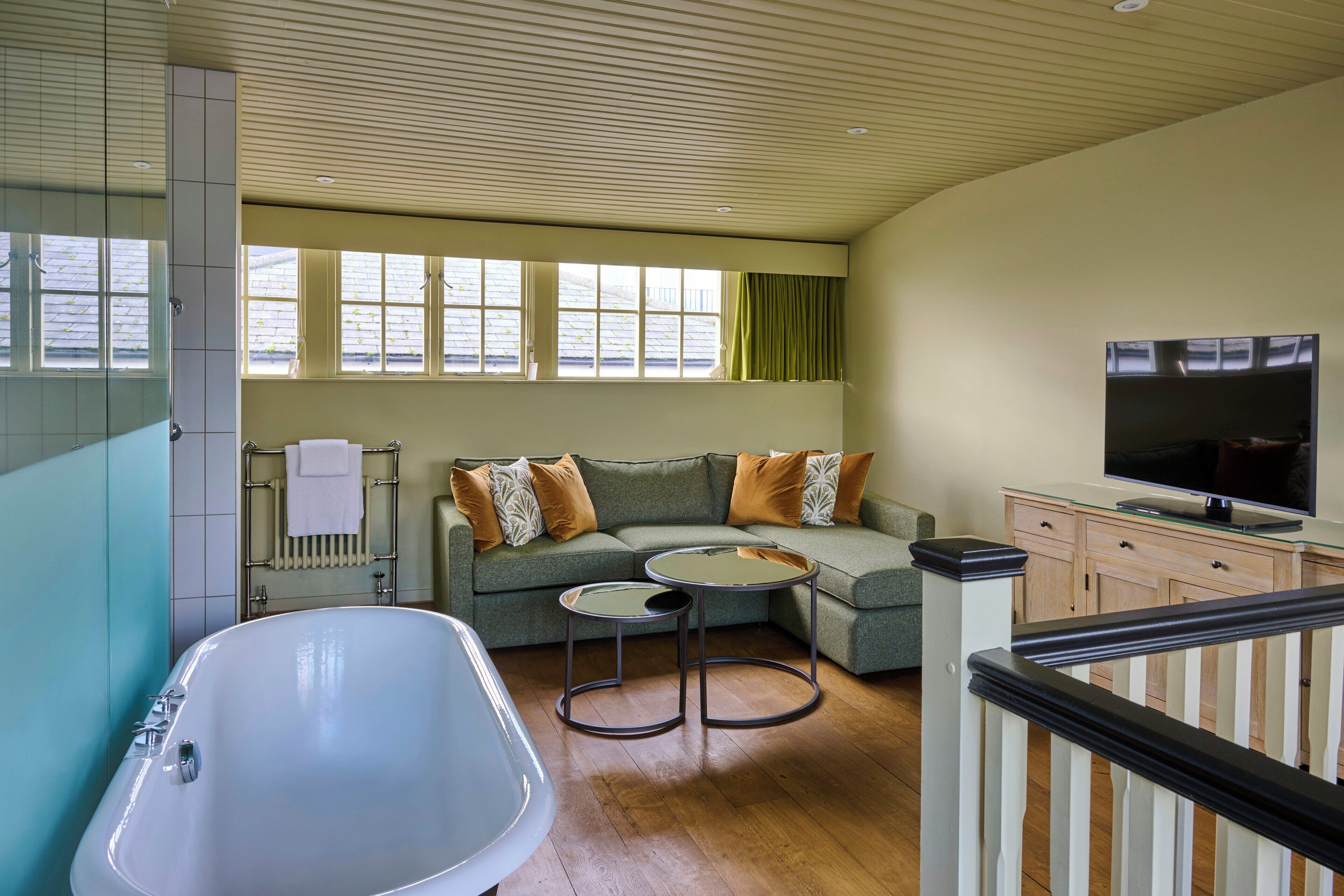 A modern living room with a large bathtub, a sectional sofa, a glass coffee table, and a flat-screen TV.