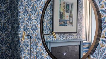A room with a patterned wallpaper, a framed artwork on the wall, and a round mirror reflecting part of the room.