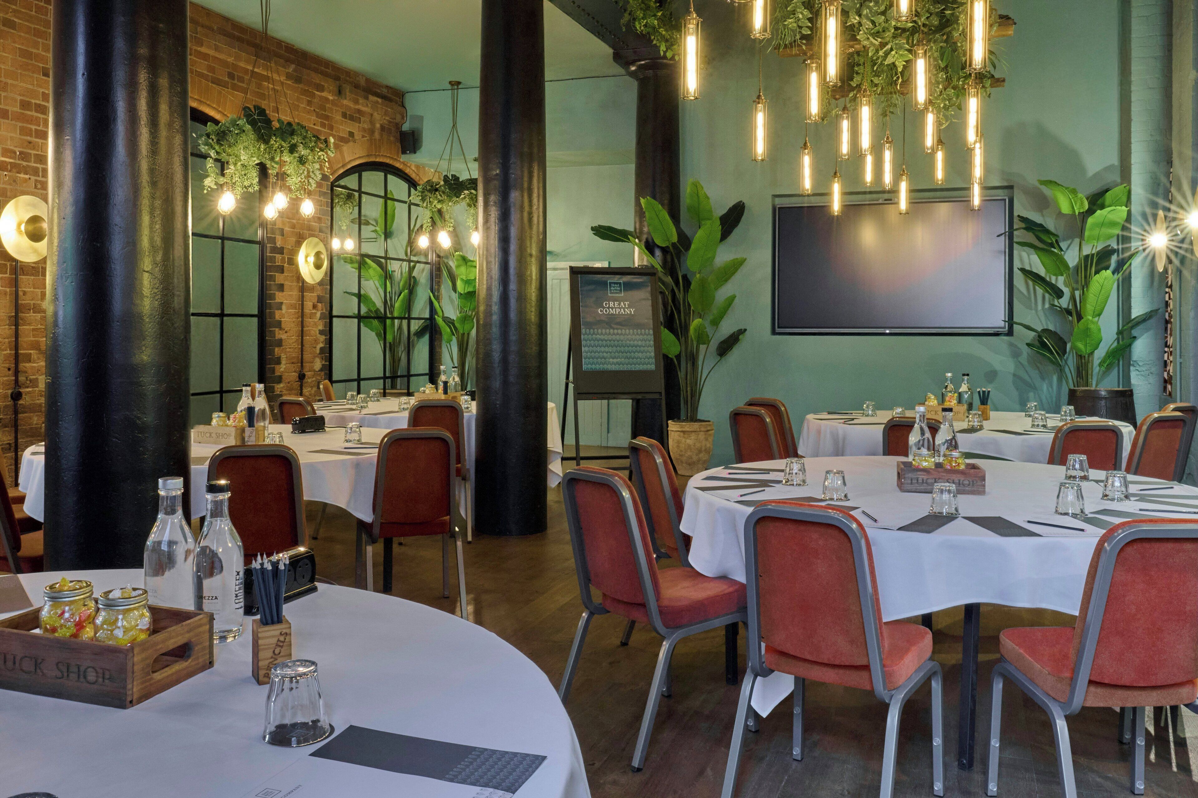 Un restaurante con mesas redondas, sillas rojas y plantas colgantes.