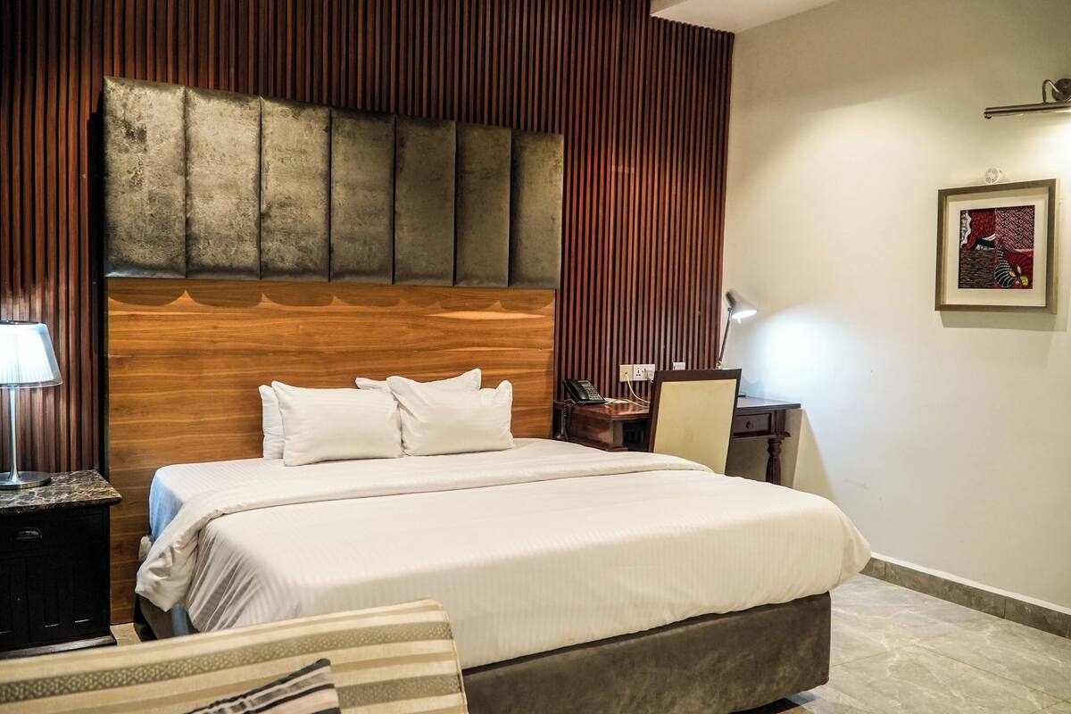 Ein Hotelzimmer mit einem großen Bett, einem Holzkopfende, einem Nachttisch mit Lampe und einem gerahmten Bild an der Wand.