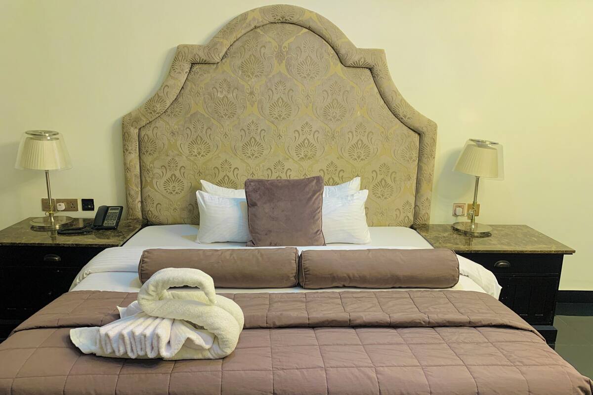 Ein Hotelzimmer mit einem großen Bett, zwei Nachttischen, einem Telefon und einem gefalteten Handtuch auf dem Bett.
