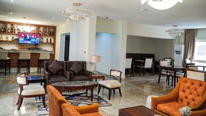 A modern hotel lobby with a bar area, seating arrangements, and a television displaying a program.