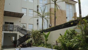 A courtyard with a ping pong table, surrounded by plants and a building with a staircase.