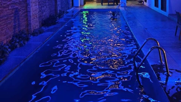A pool with a unique lighting design, a covered outdoor seating area, and a stone wall on one side.