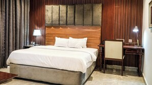 A hotel room with a large bed, a desk, a chair, and a lamp.