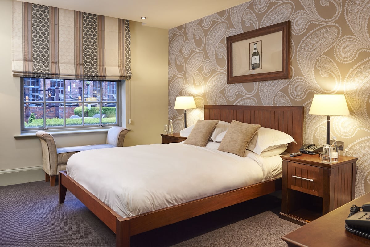 A neatly made bed with a wooden frame, two bedside tables with lamps, a chair, and a window with curtains.