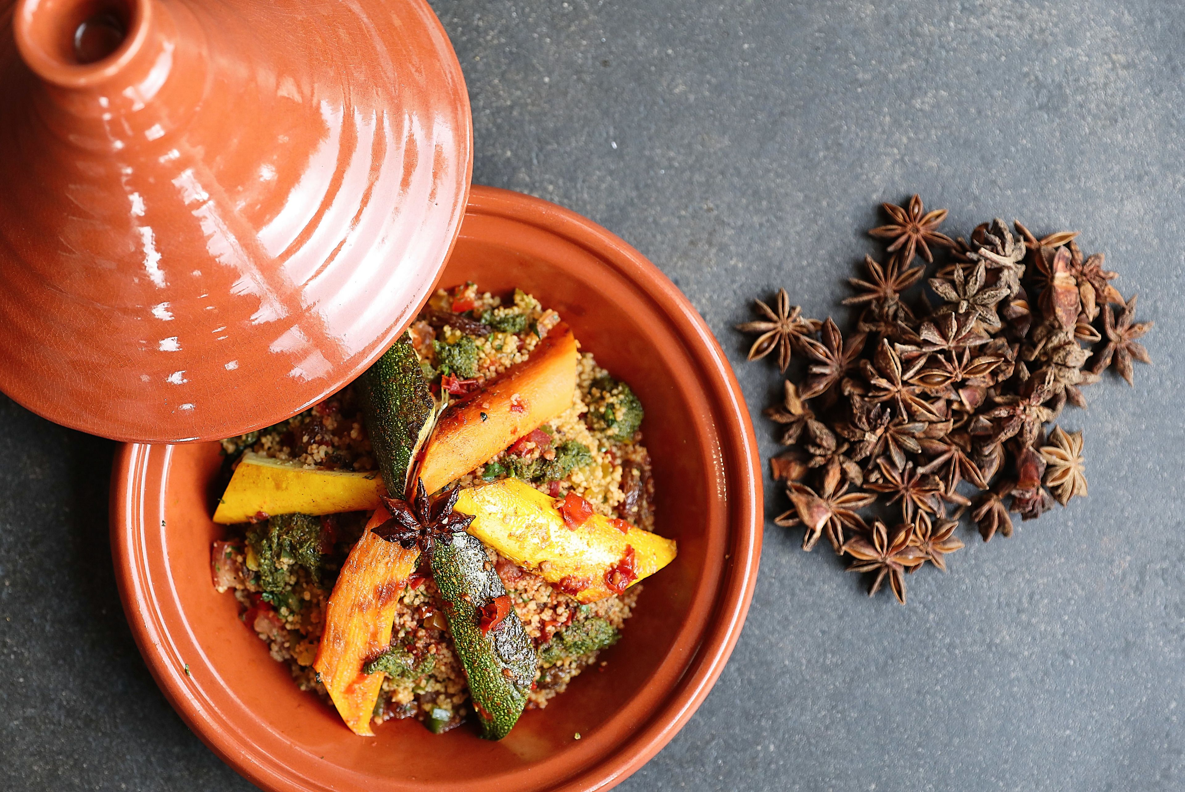 A terracotta dish with a variety of vegetables and spices, including star anise, on a dark surface.