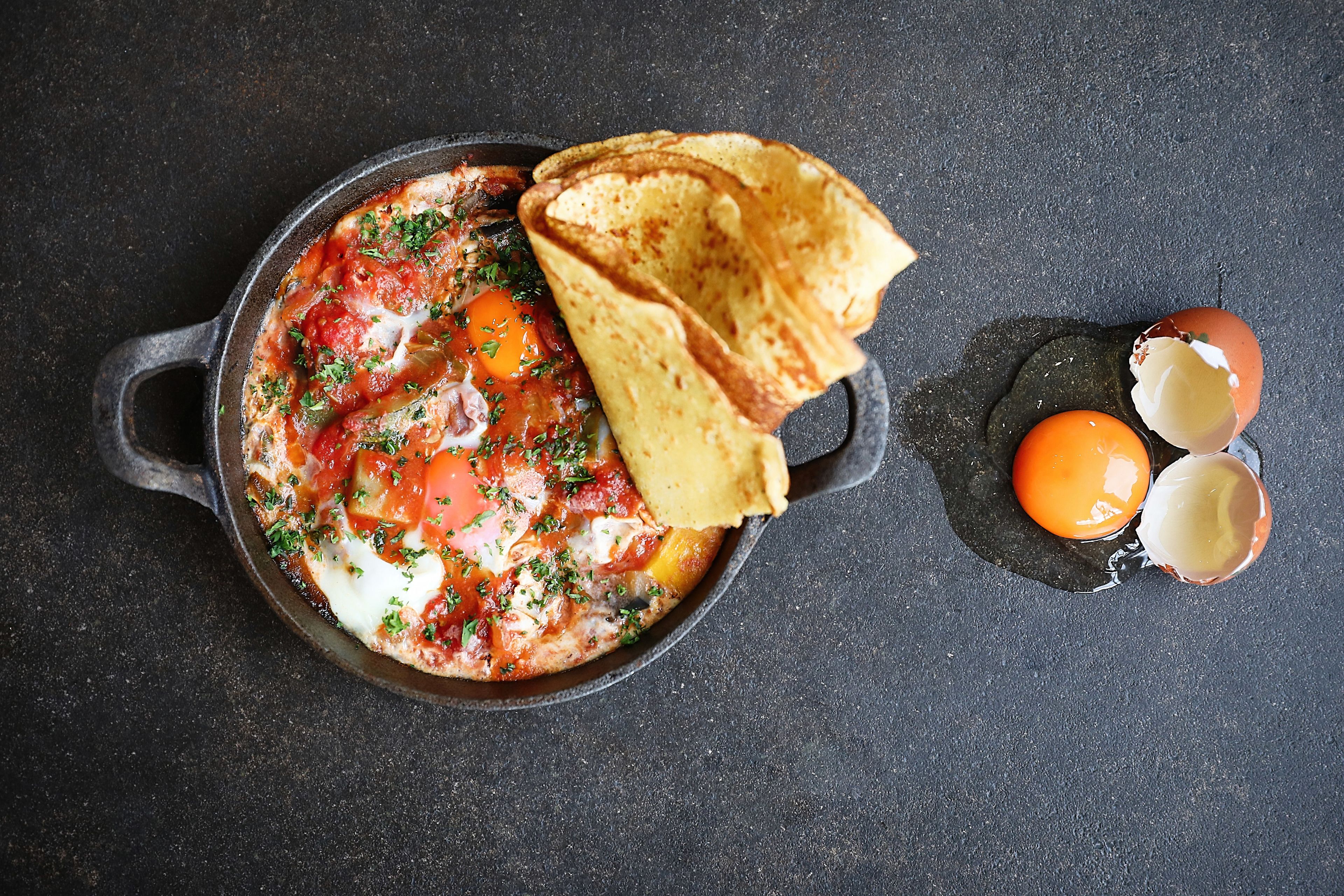 Una sartén con un guiso de tomate, acompañado de tostadas y dos huevos.