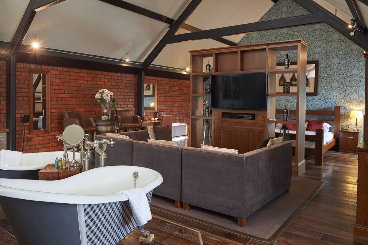 A spacious room with a large bathtub, a sofa, a television, and a brick wall.