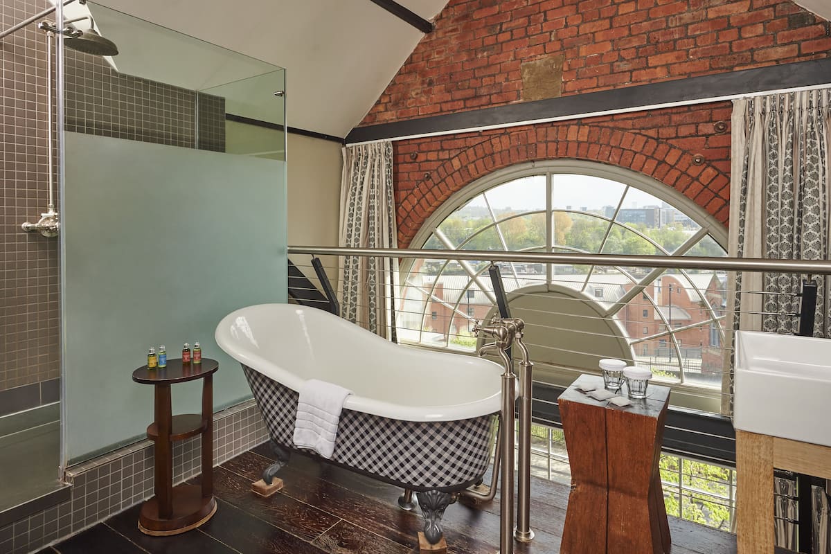 A bathroom with a freestanding bathtub, a glass-enclosed shower, and a view through a large arched window.